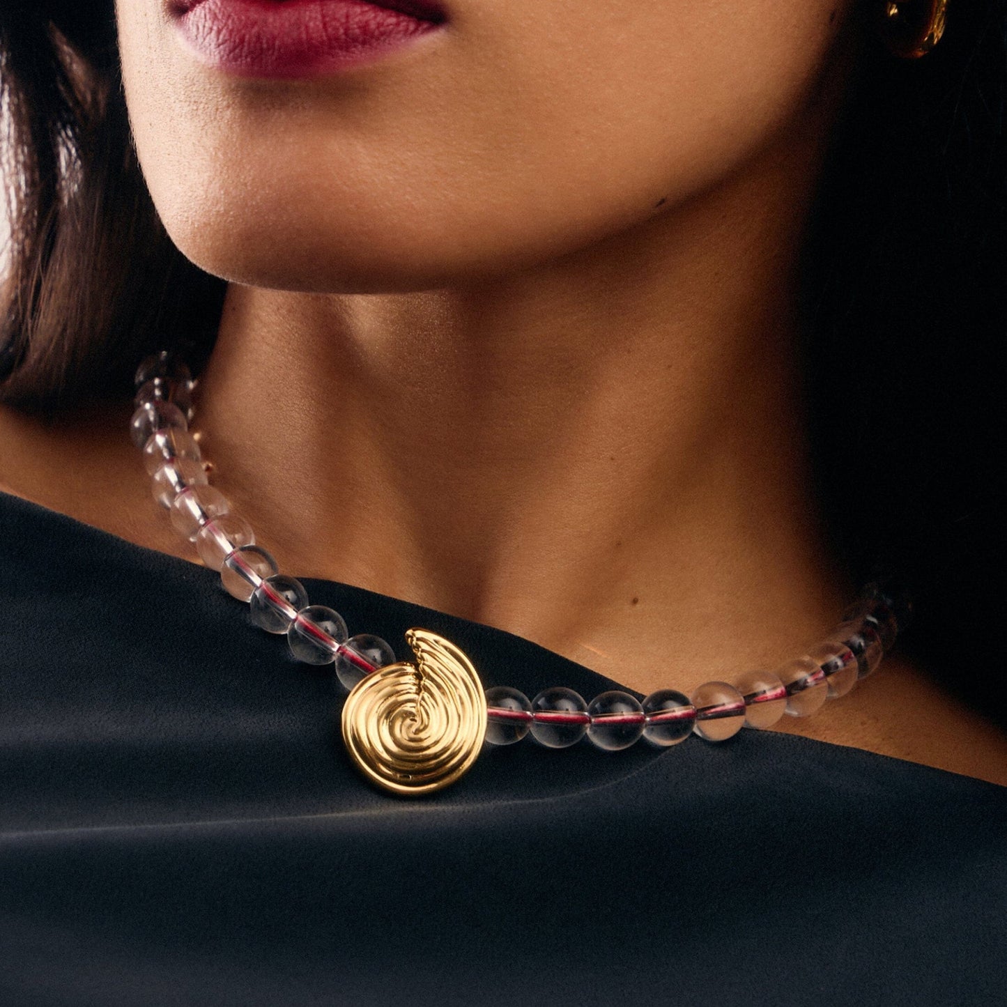 Onda Necklace with spiral wave gold pendant and clear round beads threaded by a red line — symbolizing movement and quiet energy, by MiaPromise.
